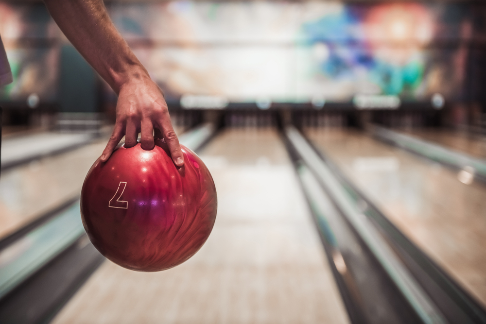 En hånd holder en blank rød bowlingkule over en treplankebane hos Hammerfest Bowling