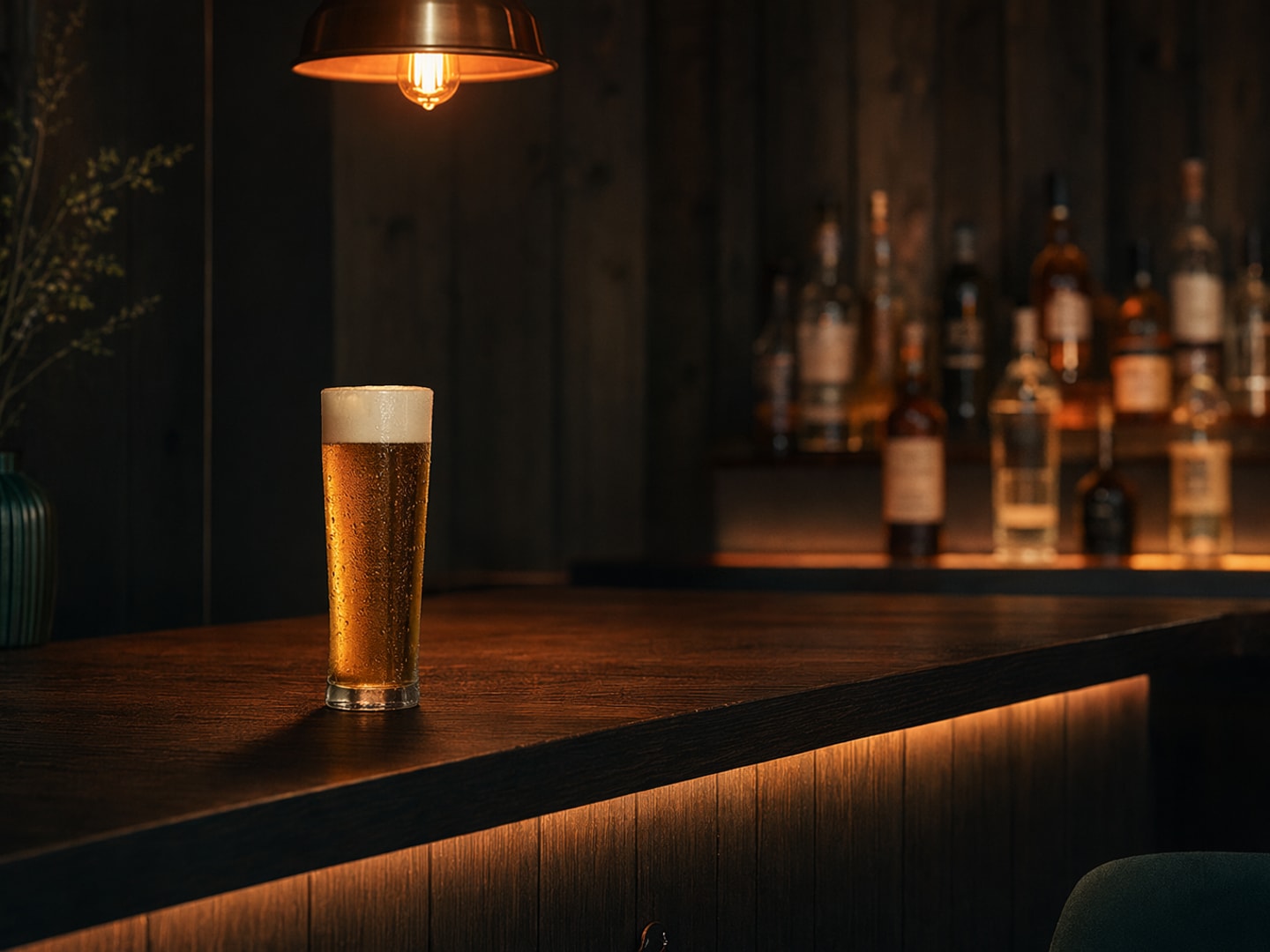 Pilsner-glass på dunkel trebar med varm pendel-belysning — Niska Bar-atmosfære